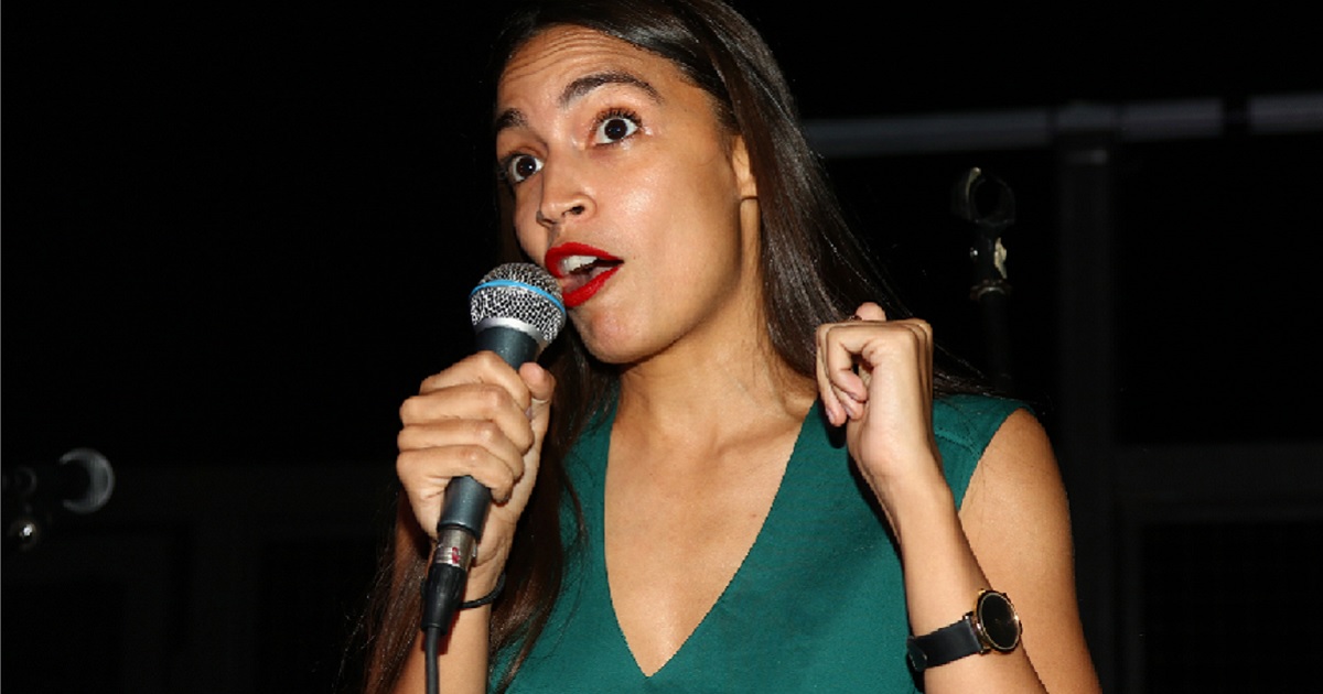 Alexandria Ocasio-Cortez holds a microphe while addressing a crowd of supporters.