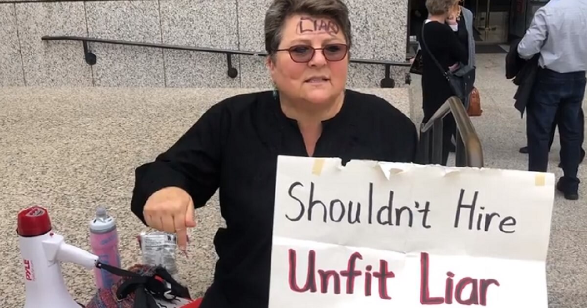 An anti-Kavanaugh protester holds a sign that says "Shouldn't hire unfit liar."