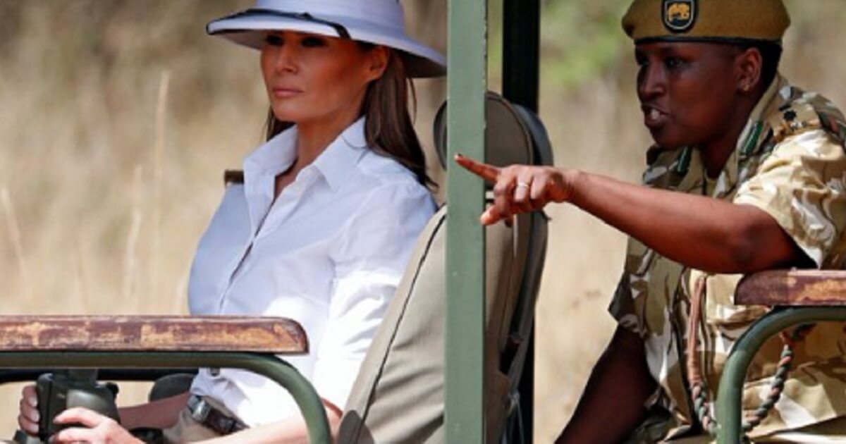 Melania Trump seated in a jeap and wearing a pitch helmet.
