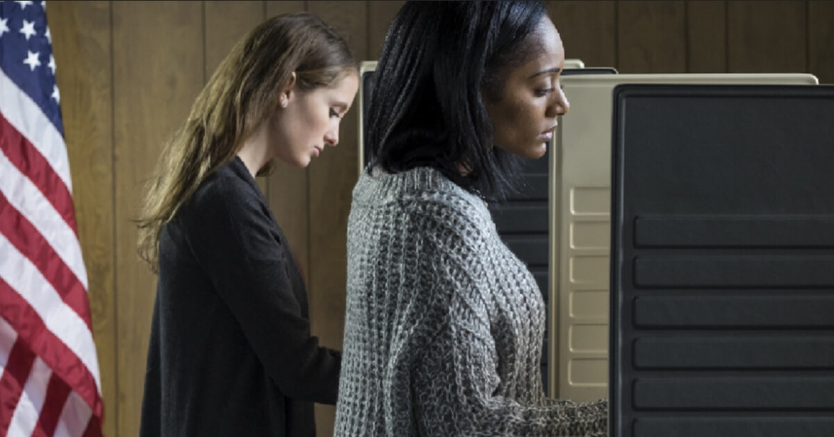 Two women, one white and one black, vote at voting booths