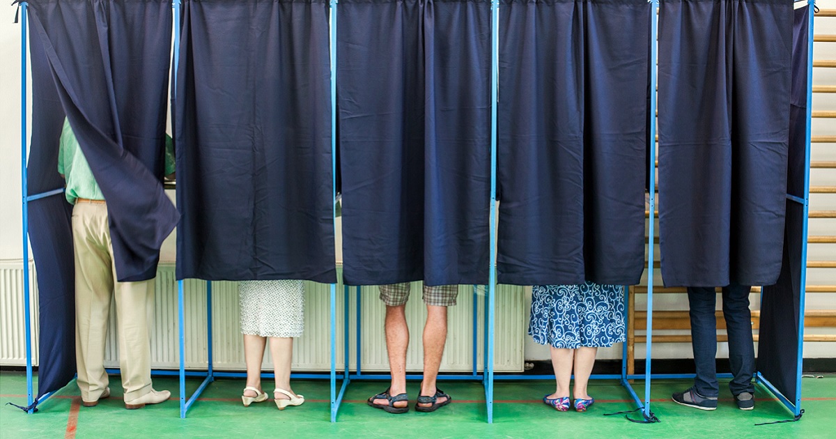 The feet of voters can be seen at the bottom of polling booths with the curtains drawn.