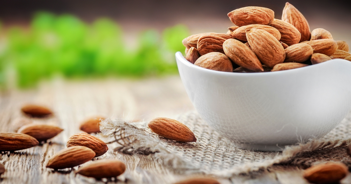 Almonds in a white porcelain bowl on a wooden table.