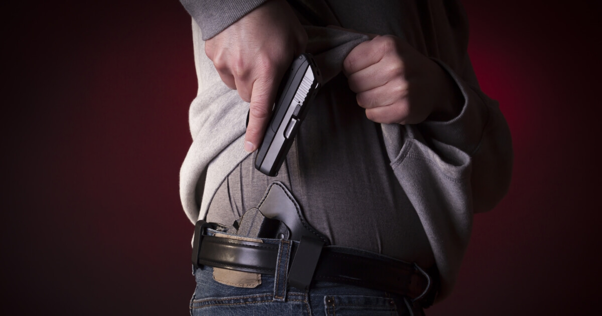 A man drawing a conceal carry pistol from an inside the waistband holster