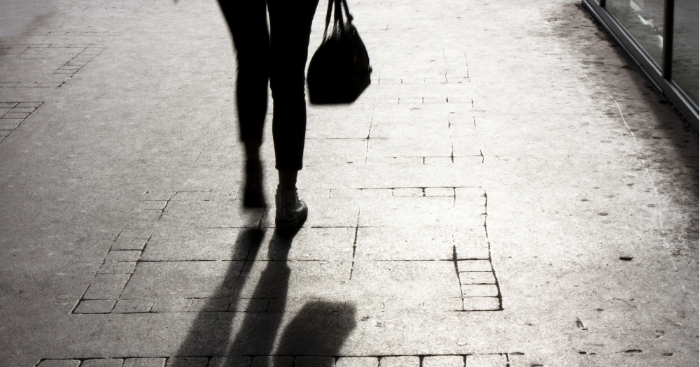 Blurry young woman with a handbag walking alone on city street, in black and white