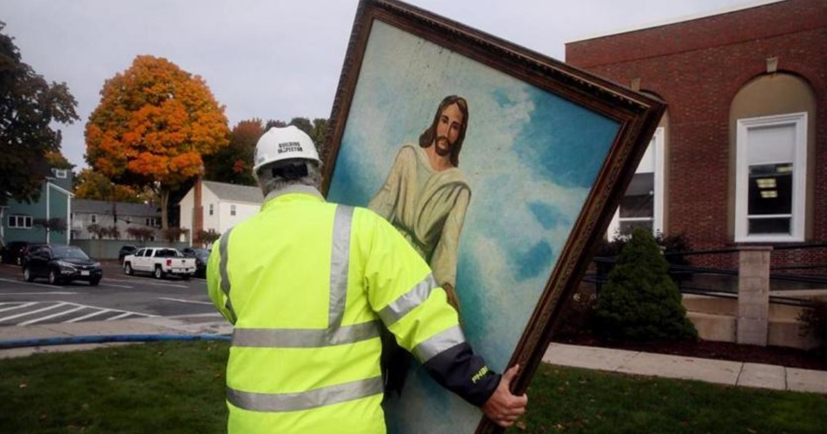 A worker carries a large painting of Jesus that survived a fire.