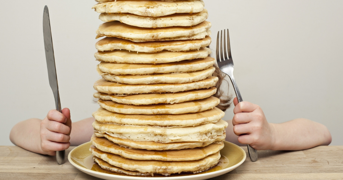 Giant stack of pancakes with a child hiding behind them.
