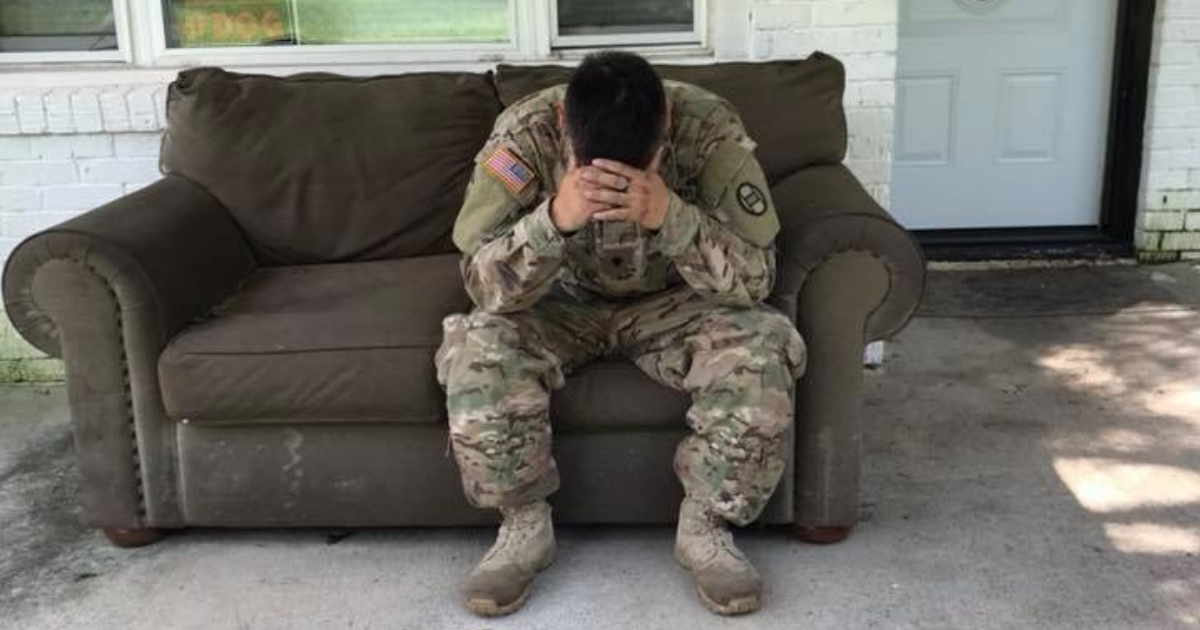A soldier sits on a couch with his head in his hands.