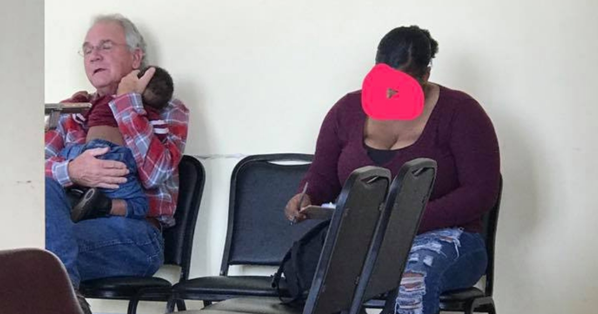 Man holding baby, left, for mom as she fills out paperwork, right.