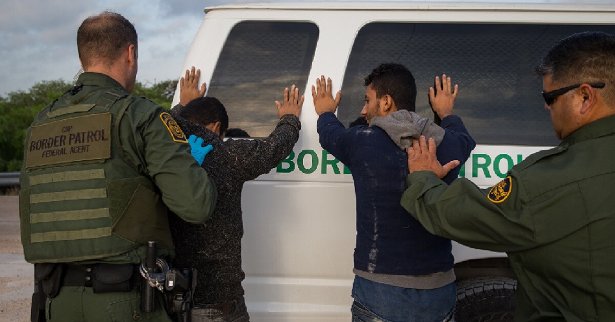 Two Border Patrol agents frisk illegal aliens against a Border Parol van.