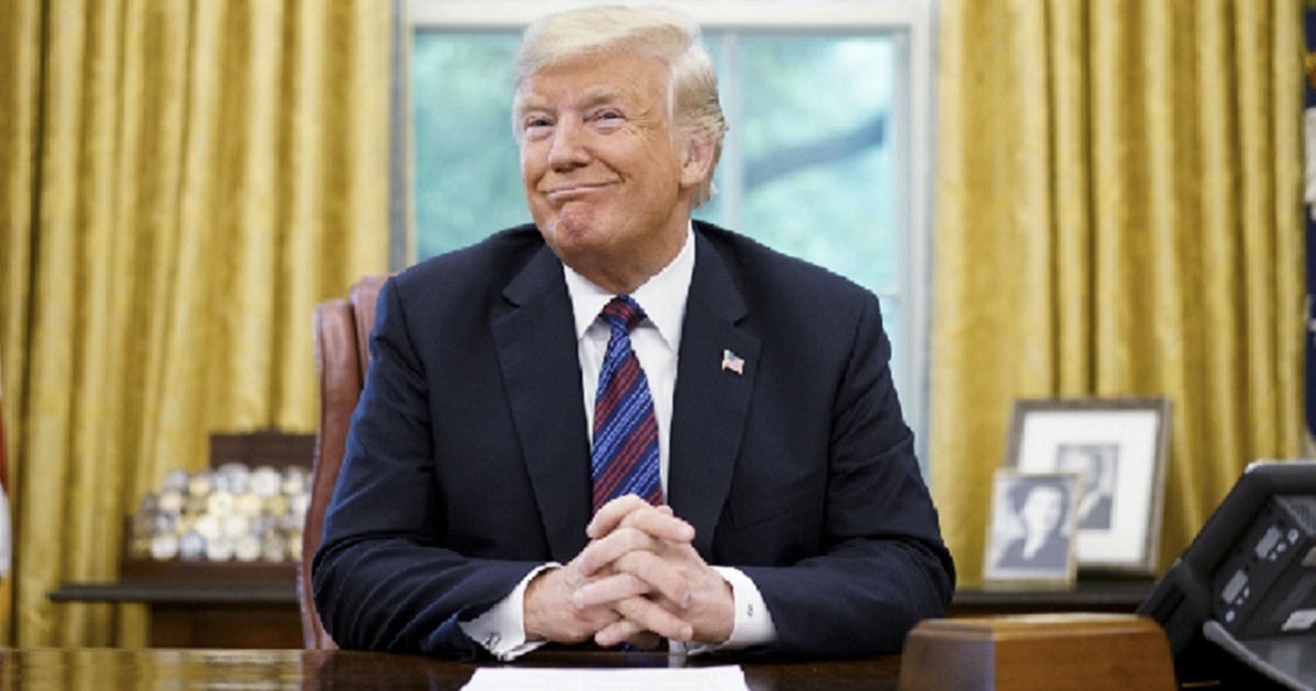 Donald Trump, seated in the Oval Office, grinning.