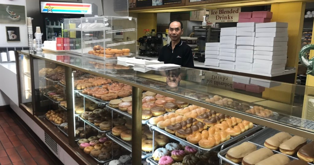 A man stands behind a counter of doughnuts.