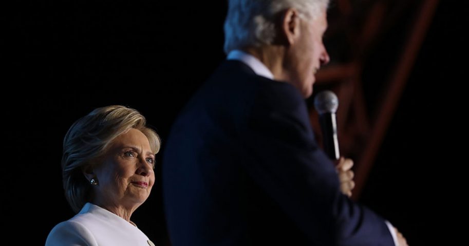 Bill Clinton speaks on stage, while Hillary Clinton looks on