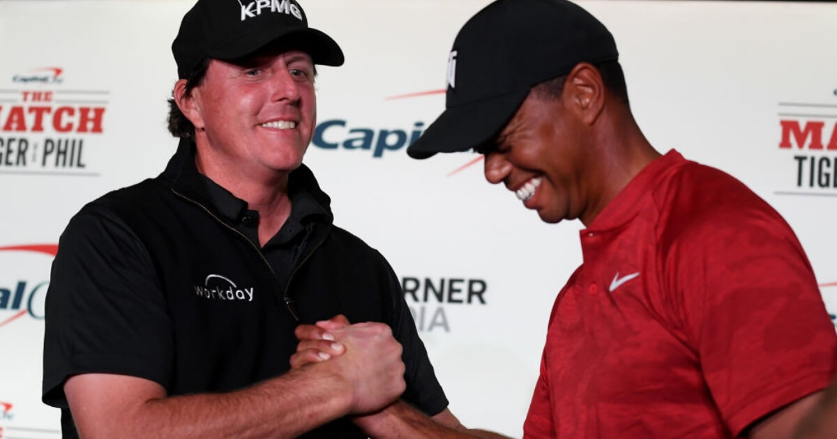 Phil Mickelson and Tiger Woods shake hands while laughing