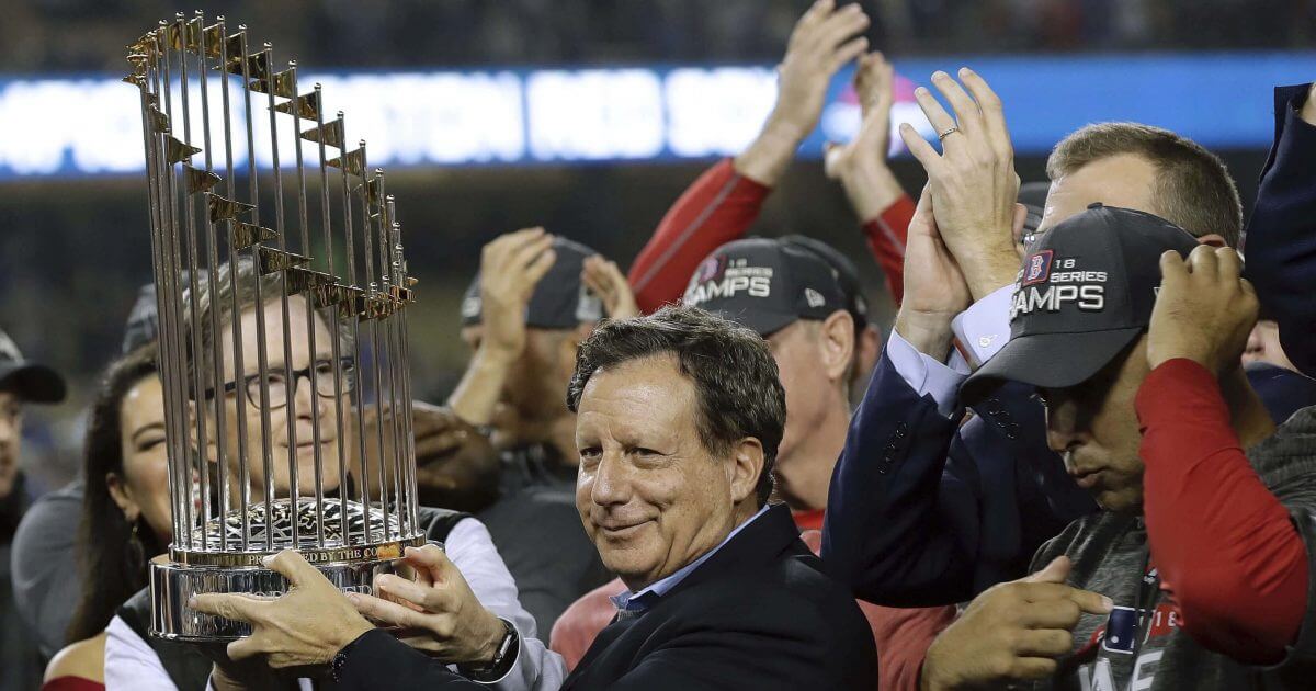 Boston Red Sox owner John Henry, partially hidden at left, and chairman Tom Werner hold the championship trophy beside manager Alex Cora, right, after Game 5 of baseball's World Series against the Los Angeles Dodgers in Los Angeles on Oct. 28, 2018.