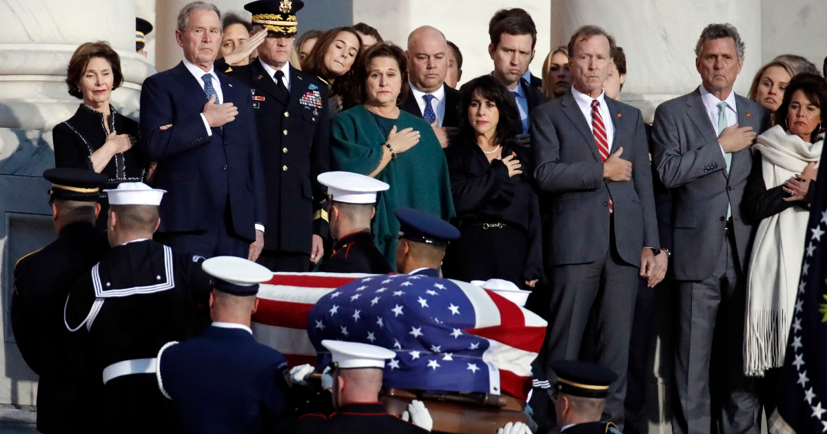 Former President George W. Bush, Laura Bush, and other family members watch as the flag-draped casket of former President George H.W. Bush is carried Monday by a joint services military honor guard to lie in state in the rotunda of the U.S. Capitol.