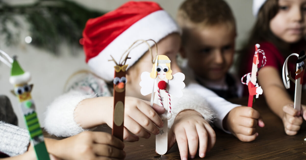 Young children holding popsicle sticks decorated for Christmas.