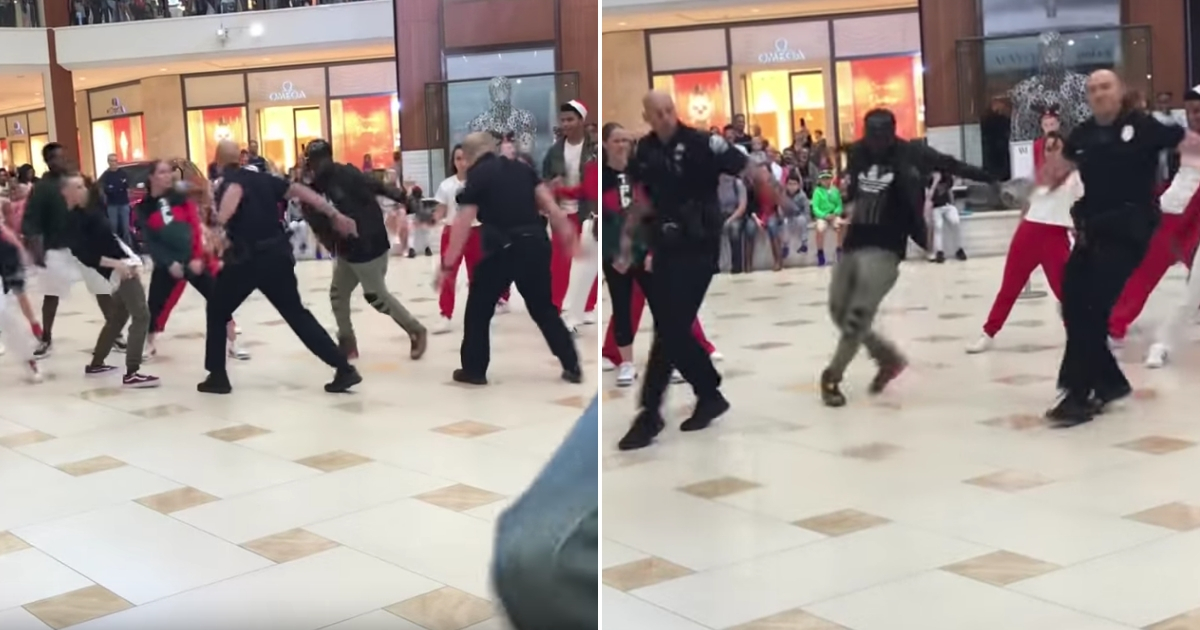 A pair of police officers dancing with a group in a mall.