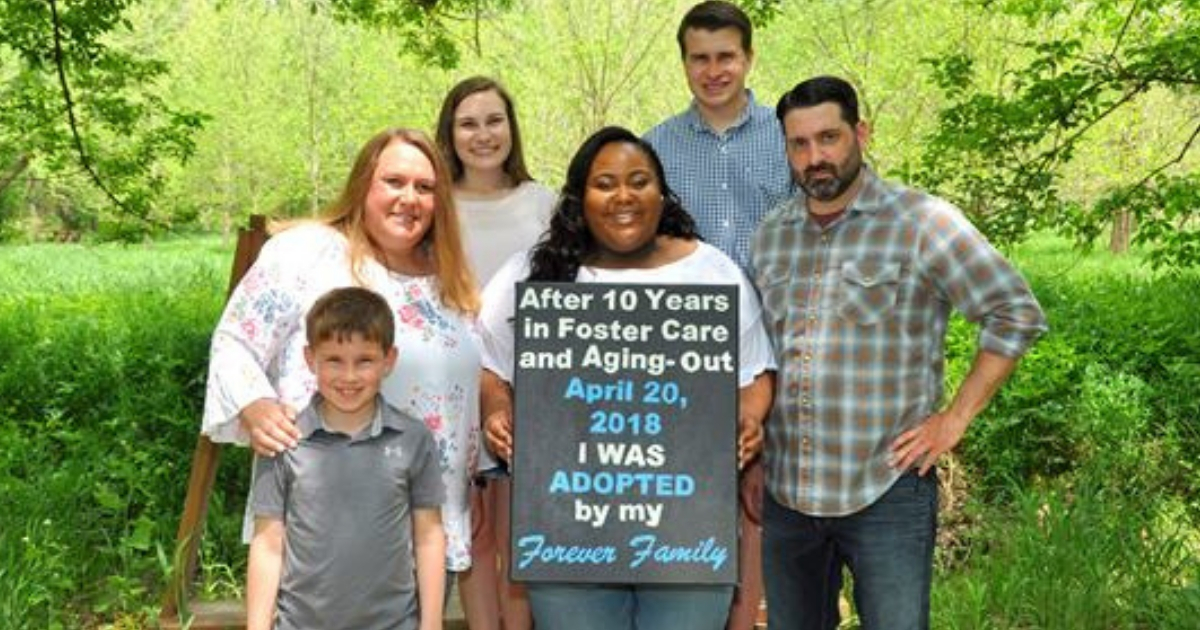 A young woman holds a sign with her new adopted family.