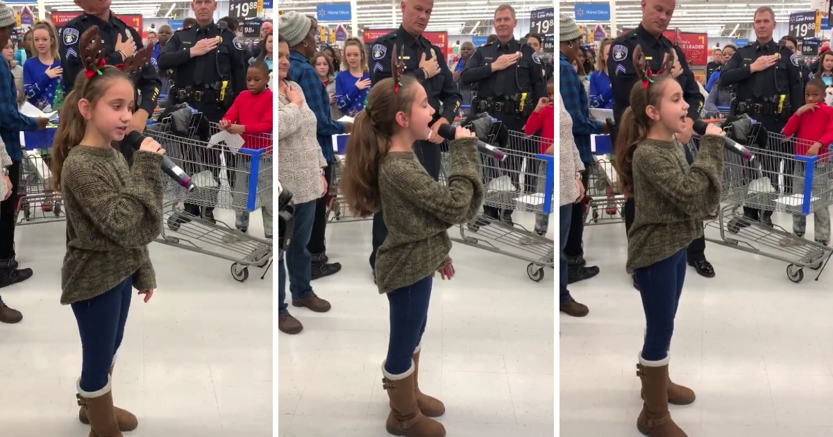 A little girl with reindeer antlers sings the national anthem inside a Walmart store.