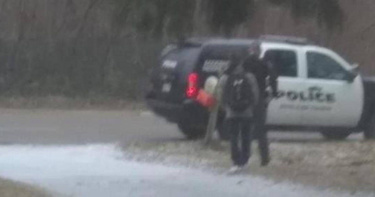 A teen walks with a police officer to the car.