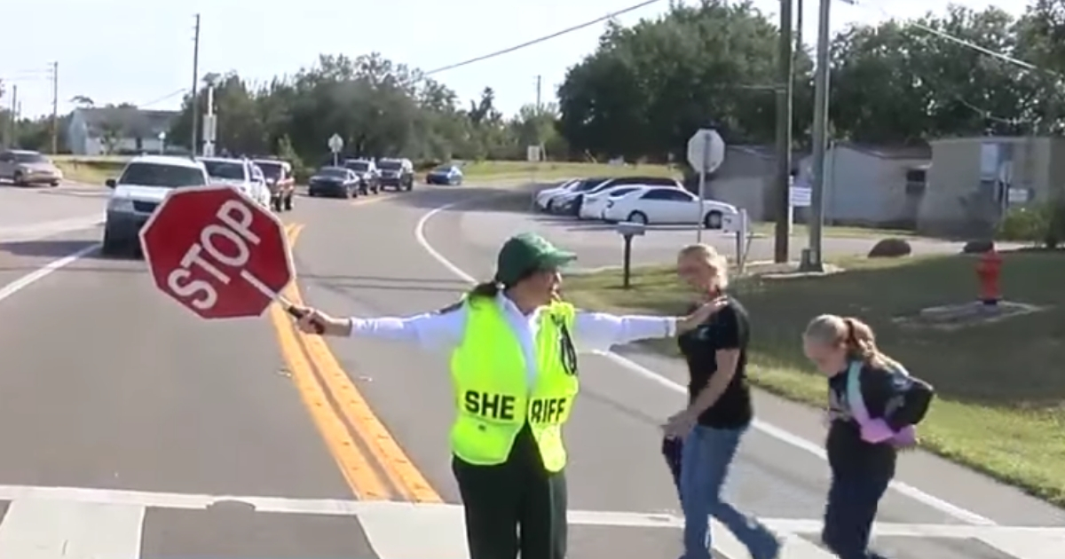 A crossing guard helps a girl and her mom across the street.