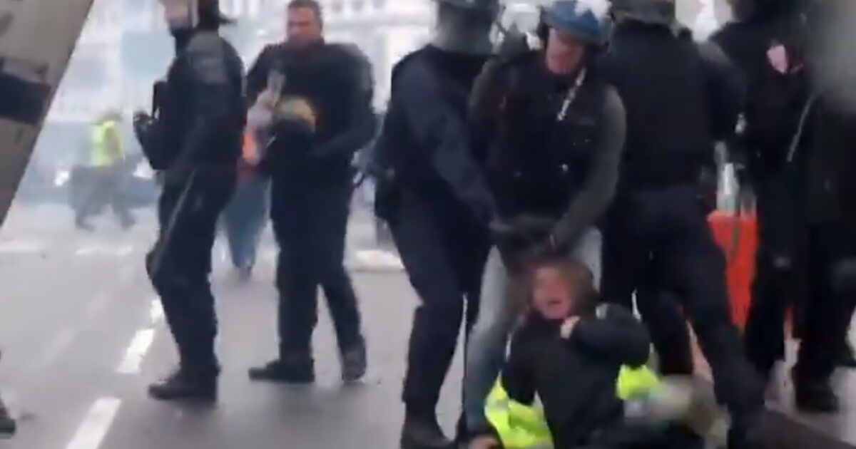 French riot police drag a woman by the hair.