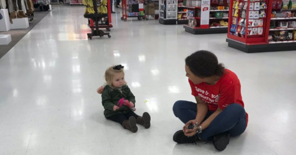 A target employee sits on the floor with a toddler.