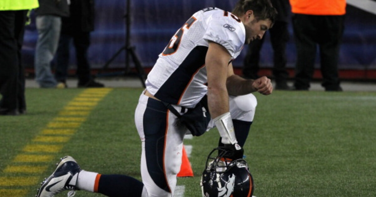 Tim Tebow kneels while on the sideline of Denver's AFC playoff game at New England in January 2012.