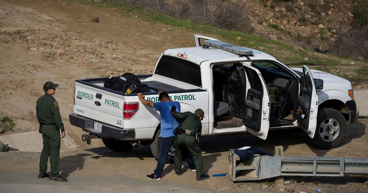 A Honduran asylum seeker is searched and taken into custody by U.S. Border Patrol agents after he crossed the U.S. border wall into San Diego, California, seen from Tijuana, Mexico, Dec. 22, 2018.