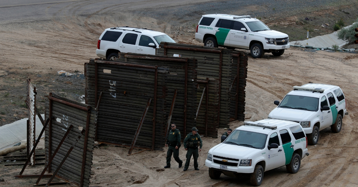 U.S. border patrol agents in San Ysidro, California respond to at least two men on the Mexican side of the U.S. border wall, one with his face covered and another holding rocks, seen from Tijuana, Mexico, Dec. 6, 2018.