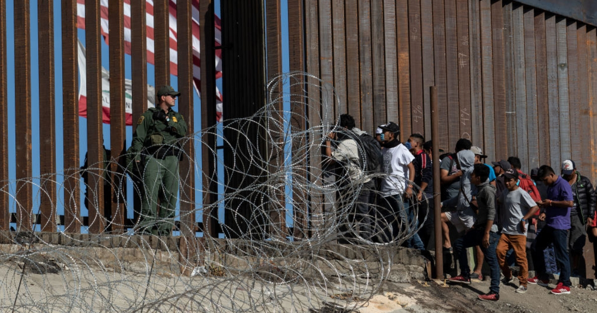 Central American migrants look through a border fence as a U.S. Border Patrol agent stands guard near the El Chaparral border crossing in Tijuana, Mexico.