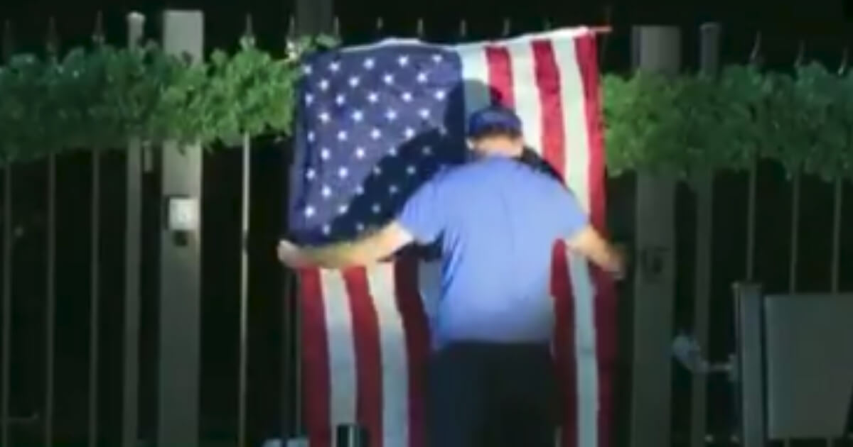 A man hangs a flag on a fence.