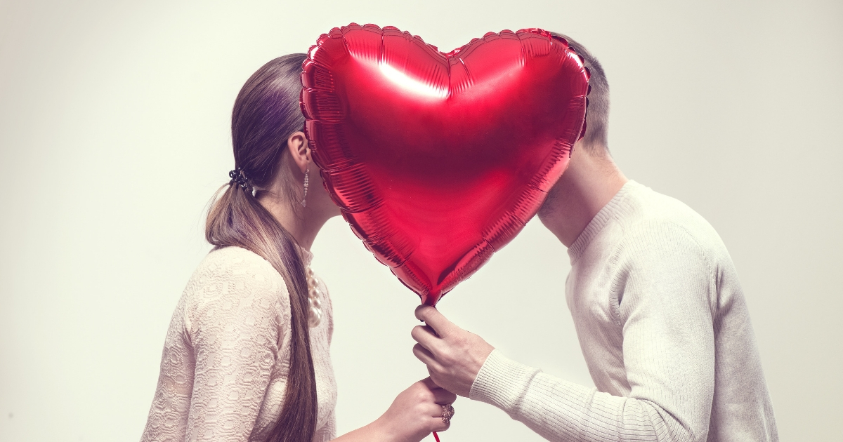 A couple kisses behind a balloon.