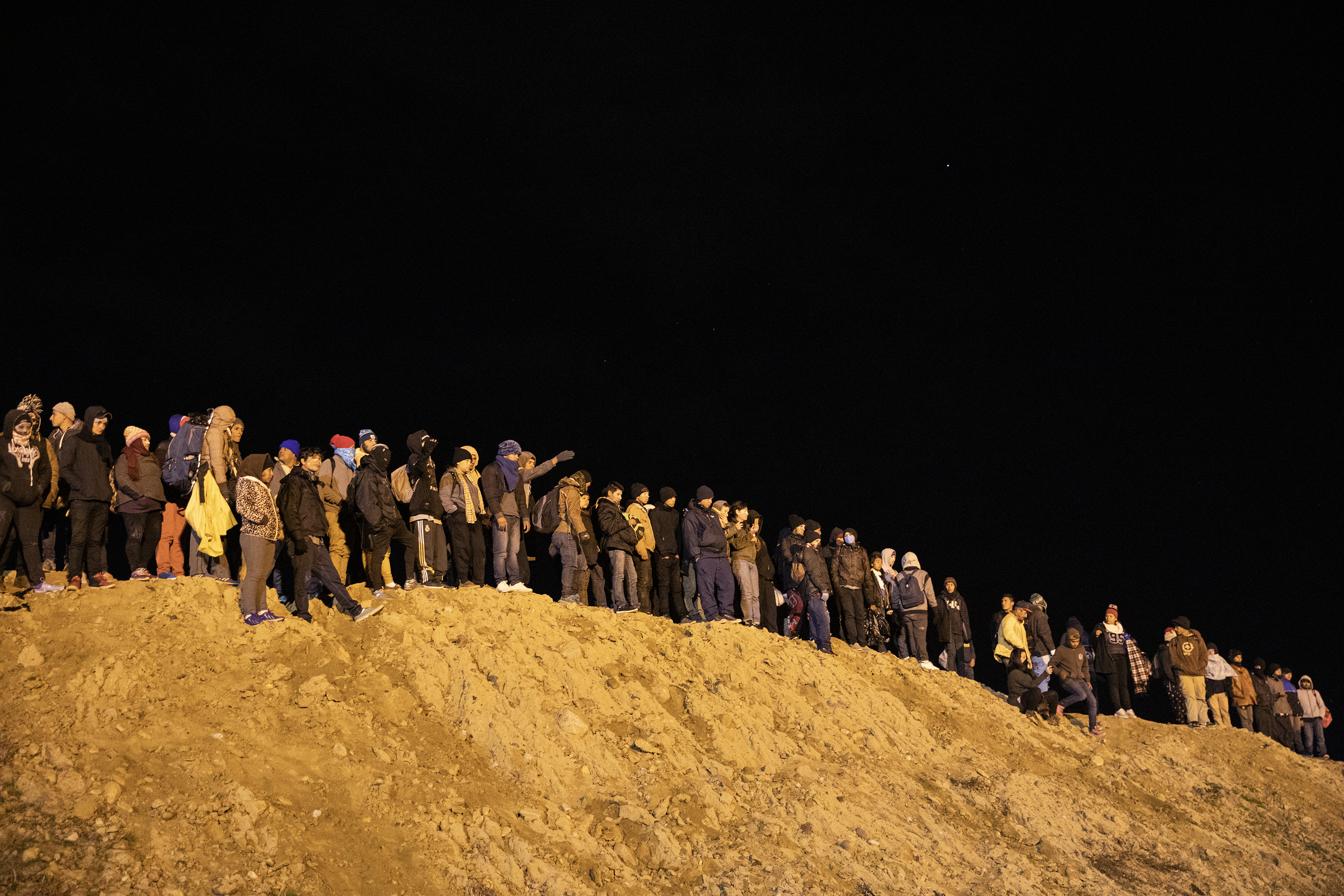 A group of Central American migrants wait to jump over the wall
