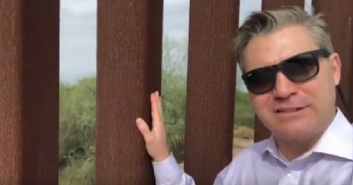 Jim Acosta next to a border barrier