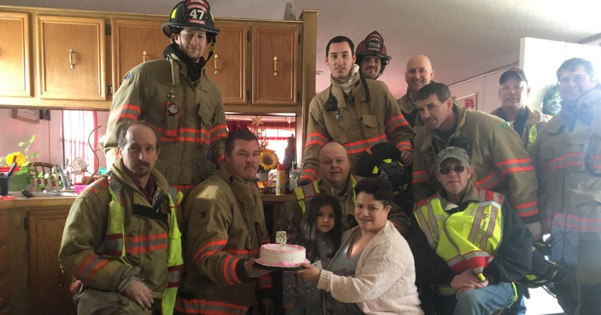 A group of firefighters pose with a little girl and her mother.