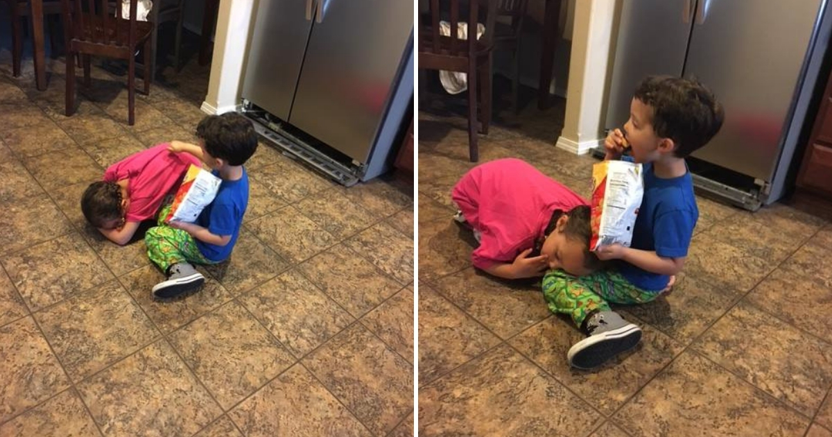 A brother and sister sitting on the kitchen floor.