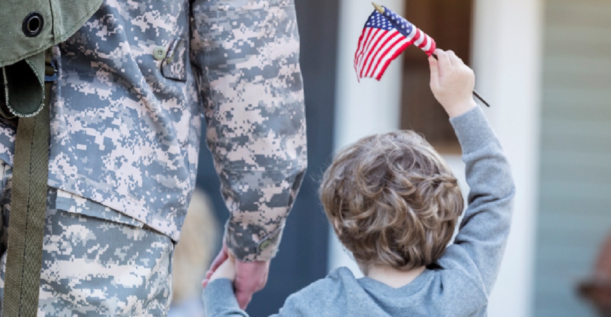 Boy carrying flag holds solder father's hand.