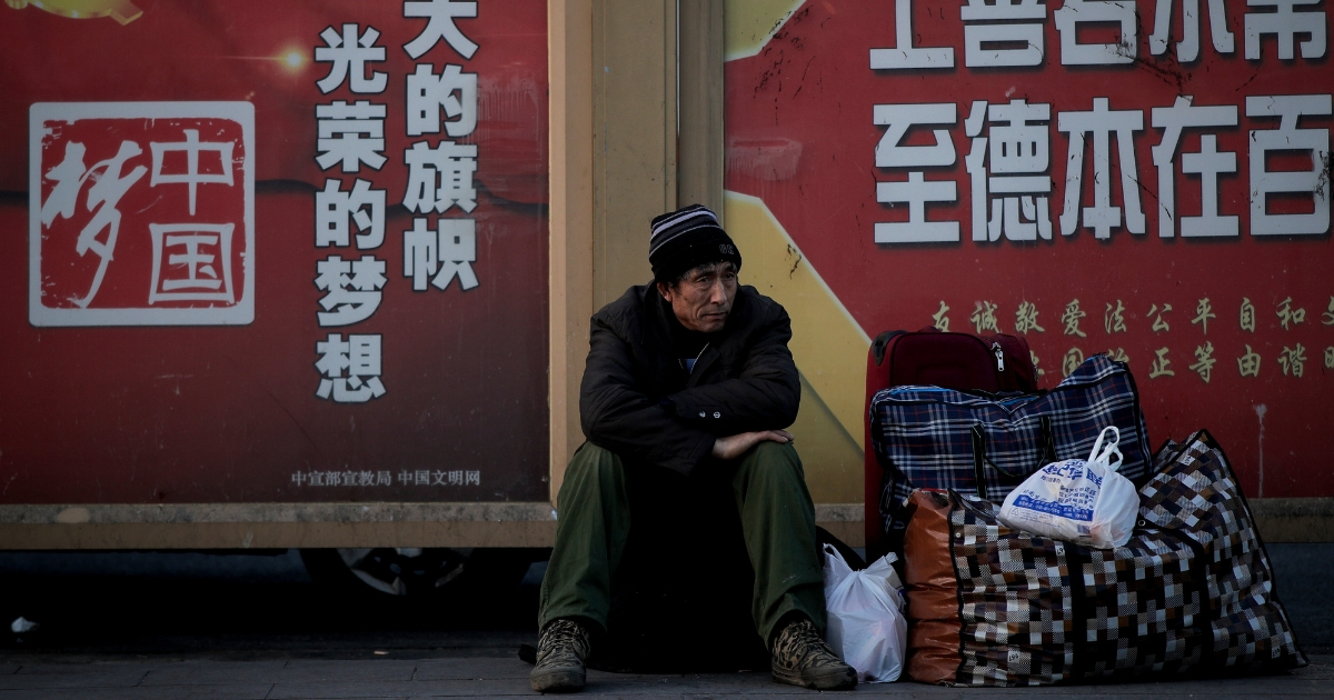 A migrant worker sits next to his belonging against a wall displaying a Chinese government propaganda message at the Beijing railway station in Beijing, Jan. 21, 2019.