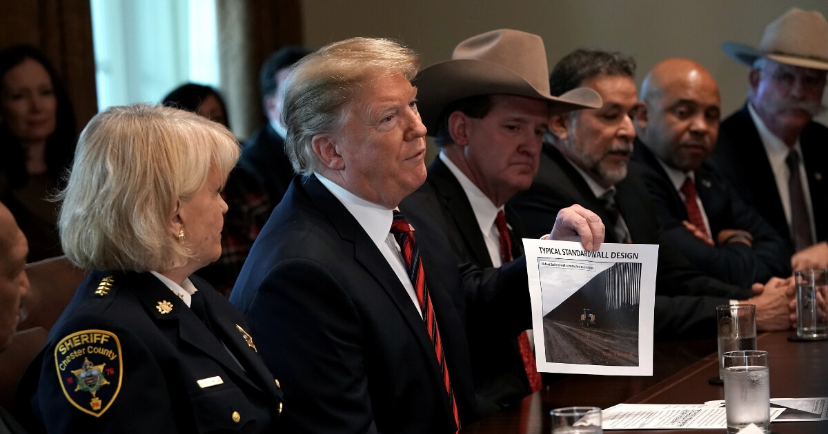 President Donald Trump holds a picture labeled 'typical standard wall design' as he hosts a round-table discussion on border security and safe communities with State, local, and community leaders in the Cabinet Room of the White House.
