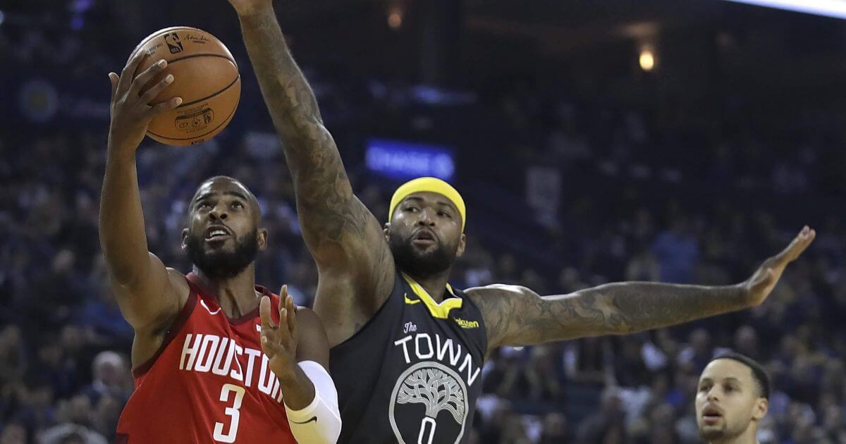 Houston Rockets point guard Chris Paul, left, lays up a shot past the Golden State Warriors' DeMarcus Cousins, center, in the first half of an NBA basketball game on Saturday, Feb. 23, 2019, in Oakland, California.