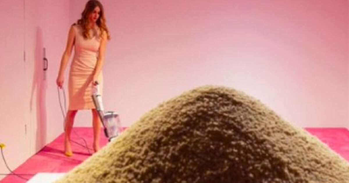 An Ivanka Trump lookalike vacuums a rug wearing a pink dress and stiletto heels.