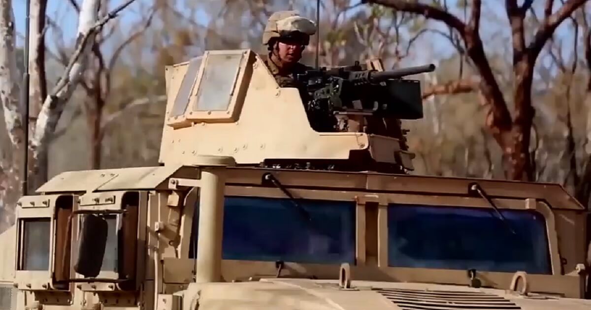 A gunner rides atop an armored military vehicle.