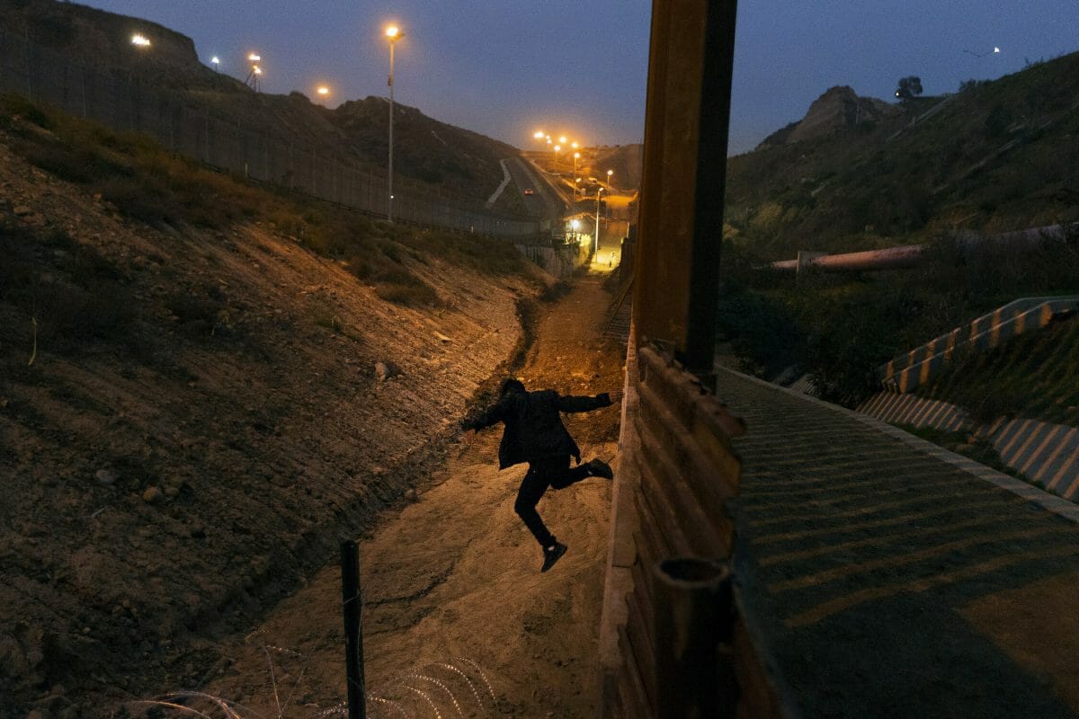 A Honduran youth jumps from the U.S. border fence in Tijuana, Mexico.