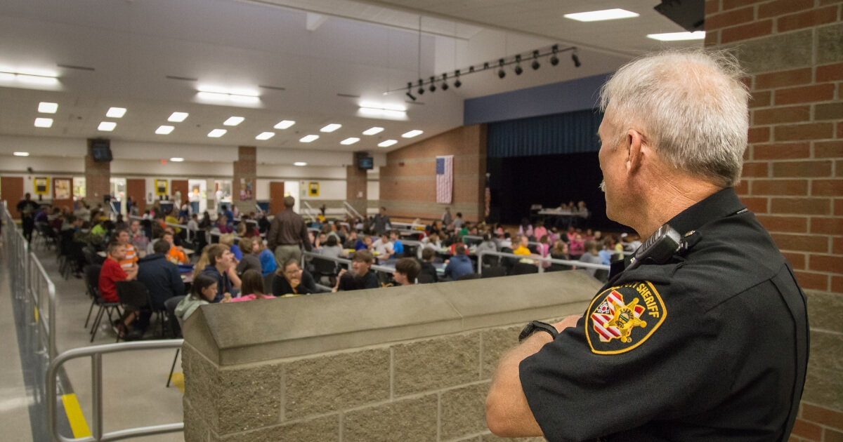 A security guard looks out over students in the cafeteria at lunch time.