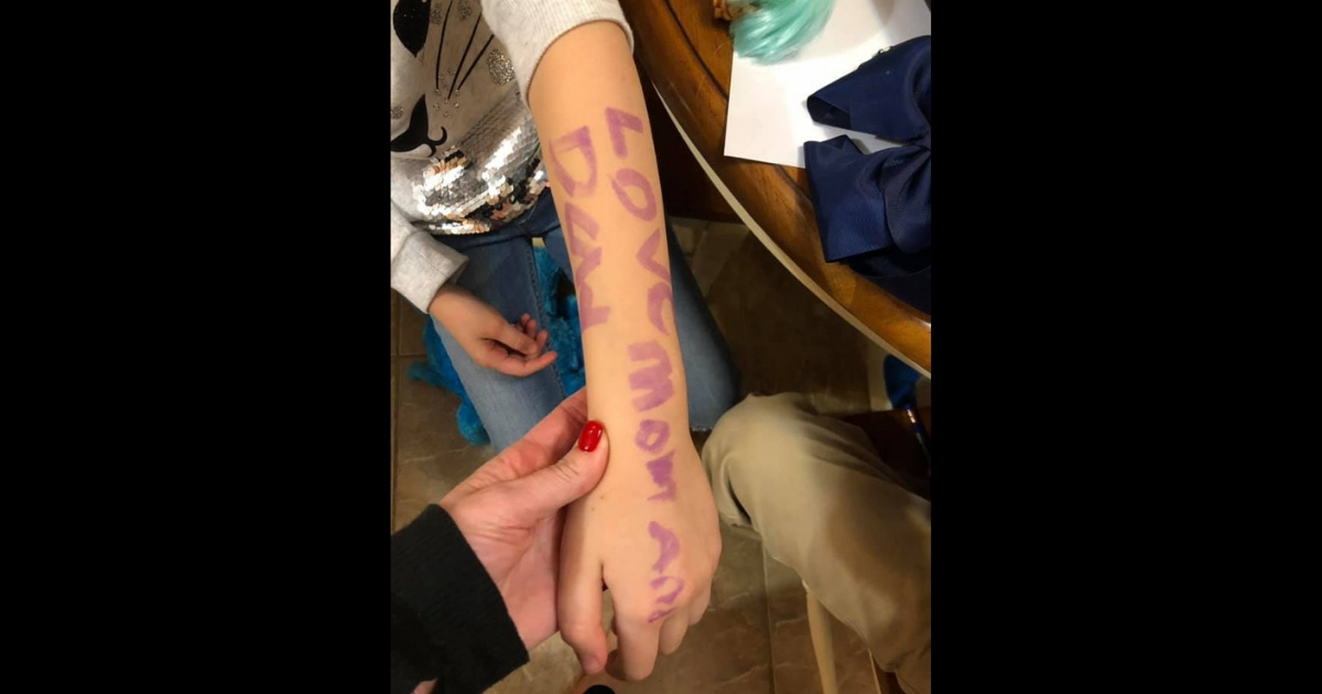 Little girl's arm with 'Love mom and dad' written on it.