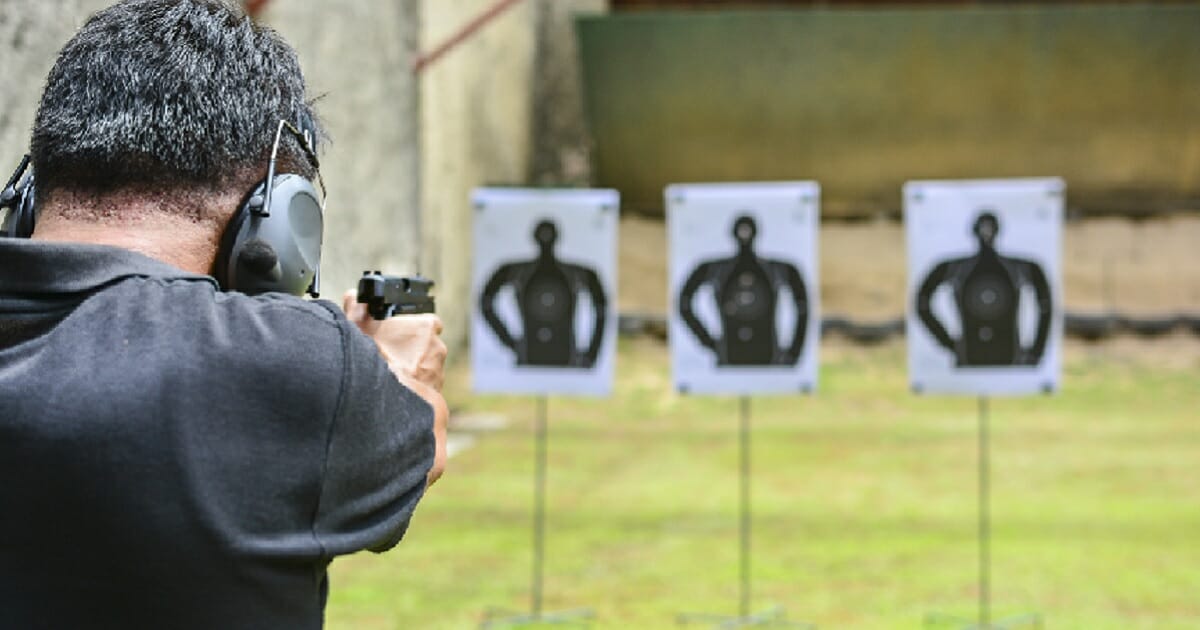 Man firing handgun at shooting range targets.