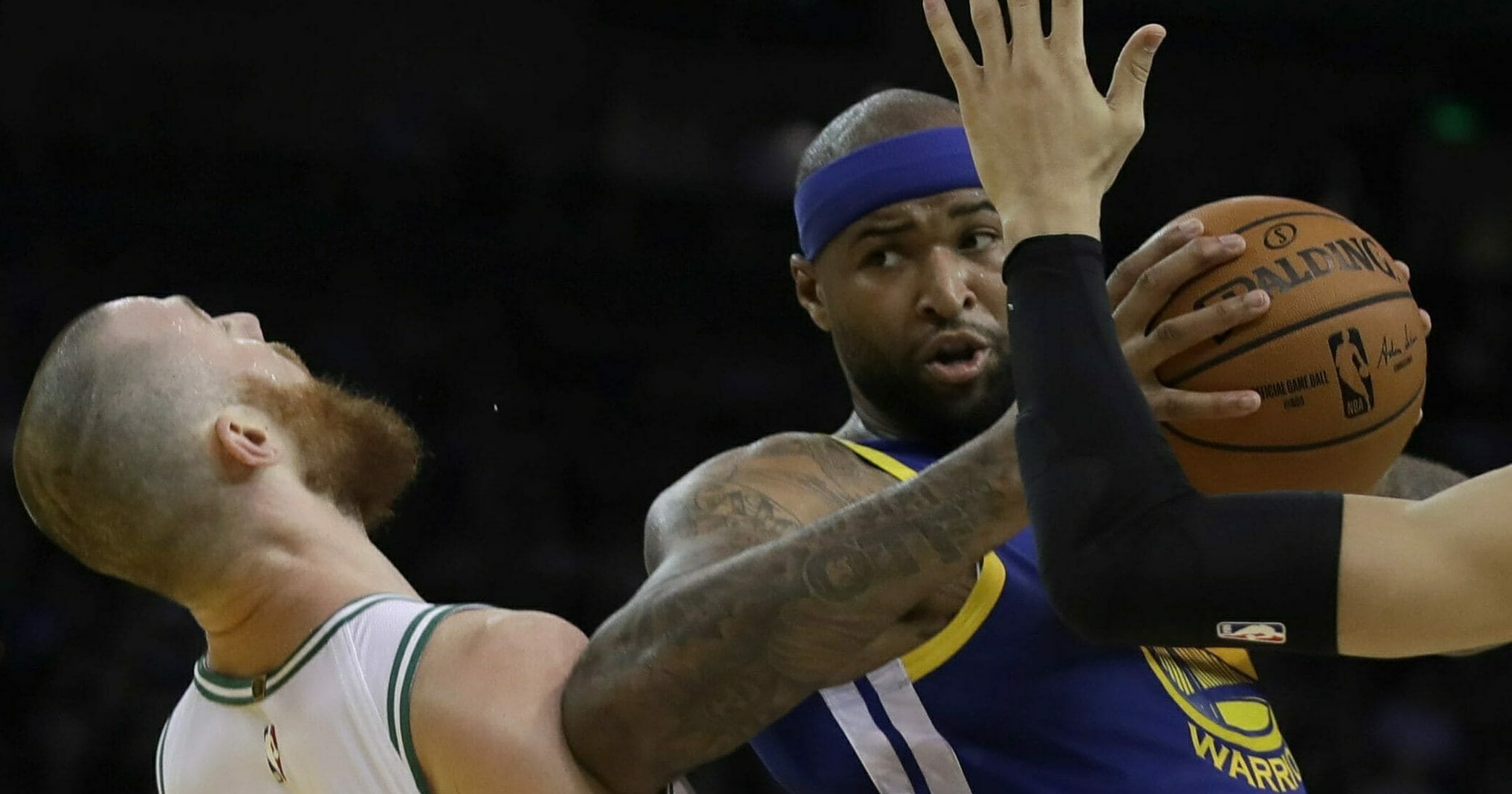 The Golden State Warriors' DeMarcus Cousins, center, fouls Boston Celtics' Aron Baynes, left, during the first half March 5, 2019, at Oracle Arena in Oakland, California.
