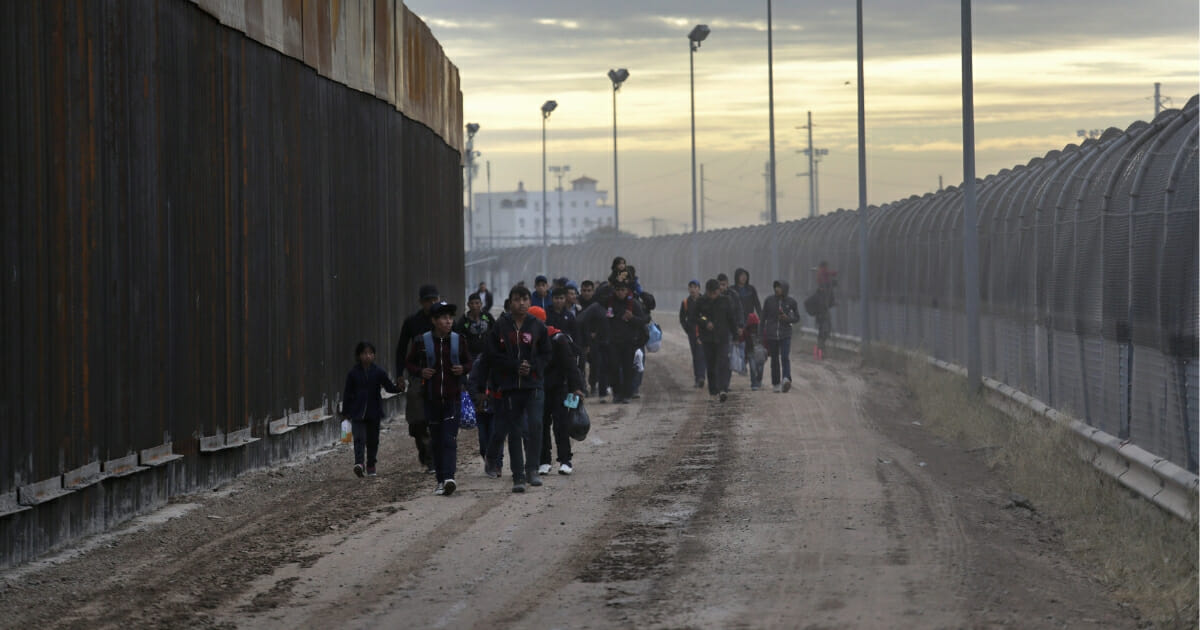 Central American immigrants walk between a newly built Bollard-style border fence