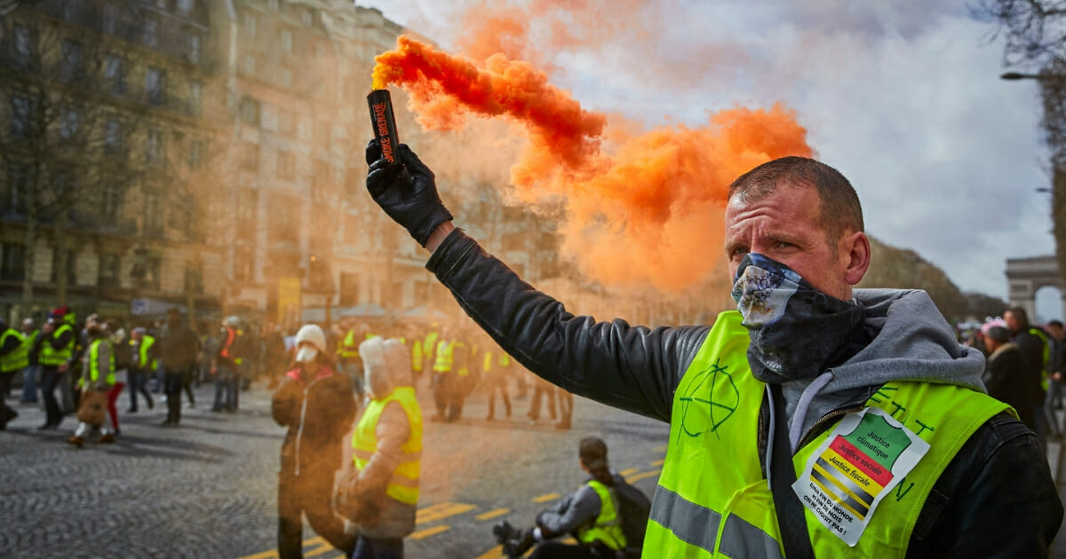Yellow Vest protestor holds an orange flare aloft during Act 17 of protests on the Champs Elysees on March 09, 2019 in Paris, France.